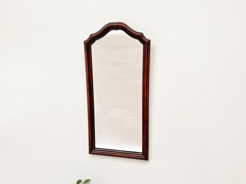 May include: A mahogany wood framed mirror with a beveled edge and an arched top.