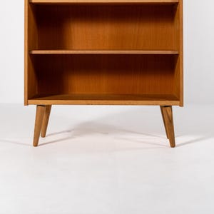 Puede incluir: Una estanter&iacute;a de madera de estilo moderno de mediados de siglo con tres estantes. La estanter&iacute;a tiene un acabado marr&oacute;n claro y patas anguladas. Los estantes son abiertos y el dise&ntilde;o es simple y funcional. Adecuado para guardar libros y objetos decorativos.