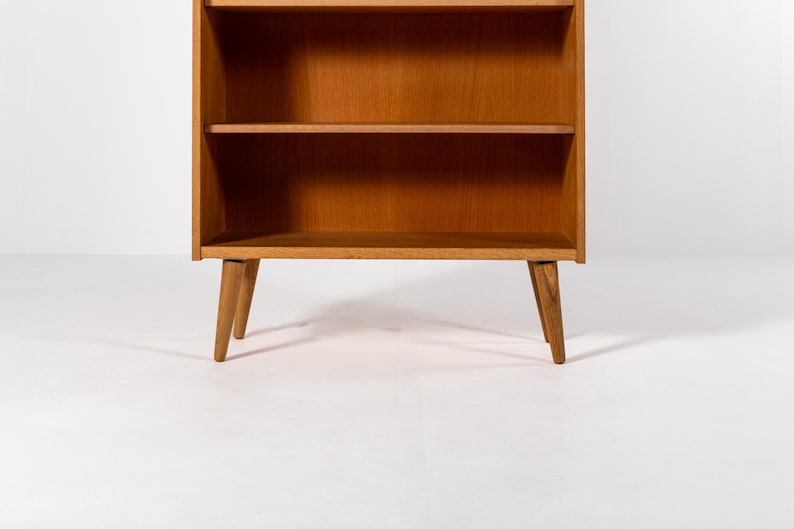 Puede incluir: Una estanter&iacute;a de madera de estilo moderno de mediados de siglo con tres estantes. La estanter&iacute;a tiene un acabado marr&oacute;n claro y patas anguladas. Los estantes son abiertos y el dise&ntilde;o es simple y funcional. Adecuado para guardar libros y objetos decorativos.
