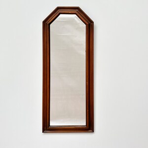 May include: A tall, rectangular mirror with a dark wood frame. The frame has a slightly arched top and a beveled edge.