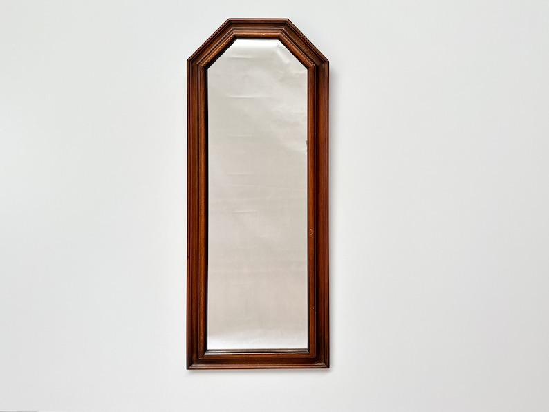 May include: A tall, rectangular mirror with a dark wood frame. The frame has a slightly arched top and a beveled edge.