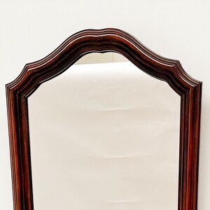 May include: A tall, rectangular mirror with a dark wood frame. The frame has a scalloped top and a smooth, polished finish.