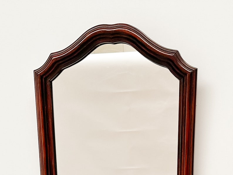 May include: A tall, rectangular mirror with a dark wood frame. The frame has a scalloped top and a smooth, polished finish.
