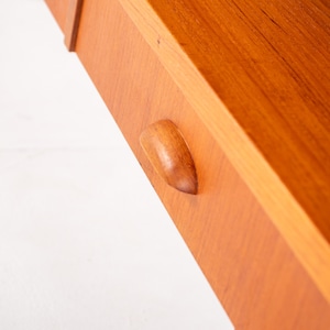 May include: Close-up of a wooden drawer with a curved handle. The drawer is made of light brown wood with visible grain and a smooth finish. The handle is a lighter shade of brown and is integrated into the drawer's design. The drawer is part of a larger wooden structure.