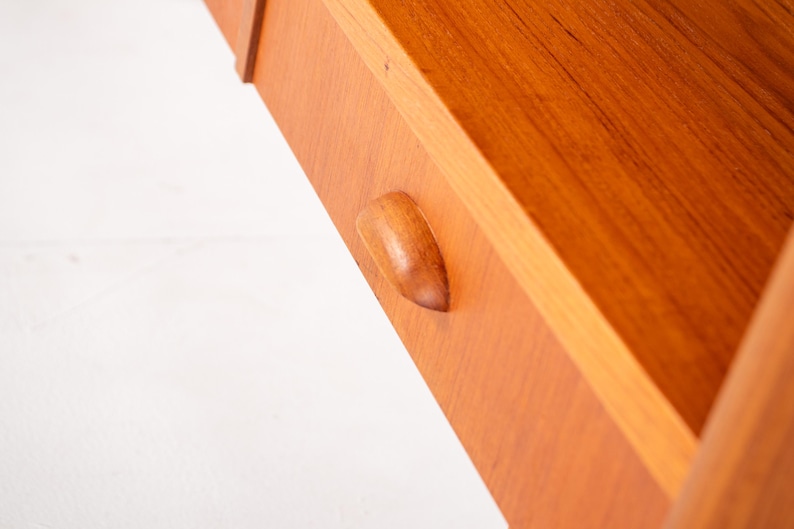 May include: Close-up of a wooden drawer with a curved handle. The drawer is made of light brown wood with visible grain and a smooth finish. The handle is a lighter shade of brown and is integrated into the drawer's design. The drawer is part of a larger wooden structure.