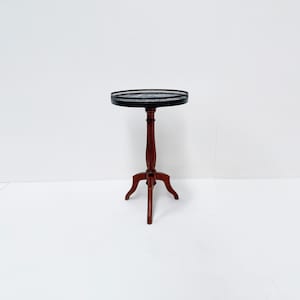 May include: A dark brown, three-legged side table with a round, black tray top. The table stands approximately 71 cm tall. The tray has a decorative edge. The table is set against a white background.