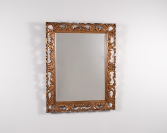 May include: A rectangular wall mirror featuring a thick, medium-brown wooden frame with intricate, carved scrollwork and leaf-like patterns along all four sides. The reflective glass surface is clear and smooth, set within the ornate, detailed border.