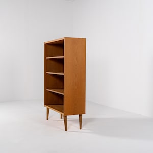 Puede incluir: Librer&iacute;a de madera de estilo moderno de mediados de siglo, con cuatro estantes. La unidad de madera marr&oacute;n claro se apoya en cuatro patas c&oacute;nicas. Los estantes abiertos ofrecen almacenamiento. El dise&ntilde;o es sencillo y funcional, adecuado para una sala de estar u oficina. Altura aproximada 120 cm.