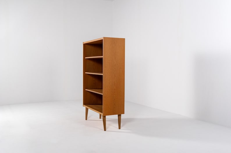 Puede incluir: Librer&iacute;a de madera de estilo moderno de mediados de siglo, con cuatro estantes. La unidad de madera marr&oacute;n claro se apoya en cuatro patas c&oacute;nicas. Los estantes abiertos ofrecen almacenamiento. El dise&ntilde;o es sencillo y funcional, adecuado para una sala de estar u oficina. Altura aproximada 120 cm.