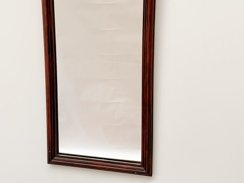 May include: A rectangular mirror with a dark wood frame. The frame has a simple, traditional design.