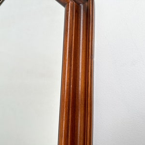 May include: Close-up of the wooden frame of a large octagonal mirror. The frame is a rich brown color and has a slightly raised edge.