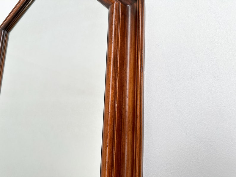 May include: Close-up of the wooden frame of a large octagonal mirror. The frame is a rich brown color and has a slightly raised edge.