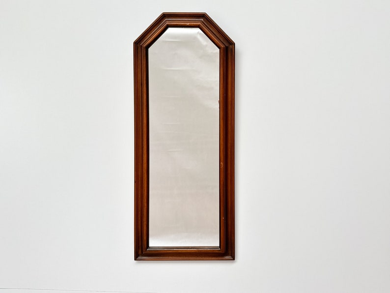 May include: A tall, rectangular mirror with a dark wood frame. The frame has a slightly arched top and a beveled edge.
