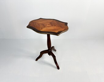 Op de afbeelding: Een kleine houten tafel met een gegolfd marquetterieblad en een driepoot onderstel. De tafel is gemaakt van donker hout en heeft een natuurlijke afwerking.