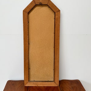 May include: A tall, rectangular wooden picture frame with a beveled edge and a light brown finish. The frame is empty and has a slightly distressed look.