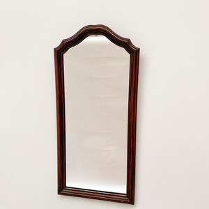 May include: A tall, rectangular mirror with a dark wood frame. The frame has a decorative, arched top with a scalloped edge.