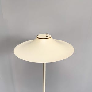 K&ouml;nnte beinhalten: Moderne, cremefarbene Stehlampe mit einem breiten, scheibenf&ouml;rmigen Schirm. Der Schirm wird von einem schlanken, geraden Pfosten getragen. Das Design der Lampe ist minimalistisch und elegant, passend f&uuml;r moderne Innenr&auml;ume.
