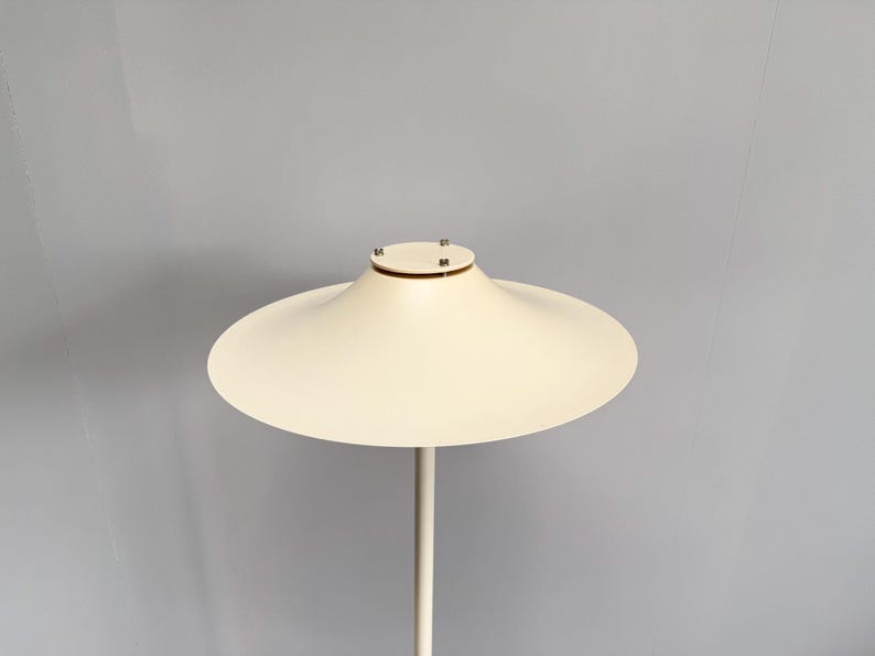 K&ouml;nnte beinhalten: Moderne, cremefarbene Stehlampe mit einem breiten, scheibenf&ouml;rmigen Schirm. Der Schirm wird von einem schlanken, geraden Pfosten getragen. Das Design der Lampe ist minimalistisch und elegant, passend f&uuml;r moderne Innenr&auml;ume.