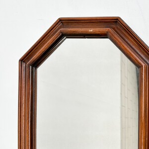 May include: A wooden octagonal mirror with a simple, elegant design. The mirror has a dark brown wood frame and a clear glass surface.