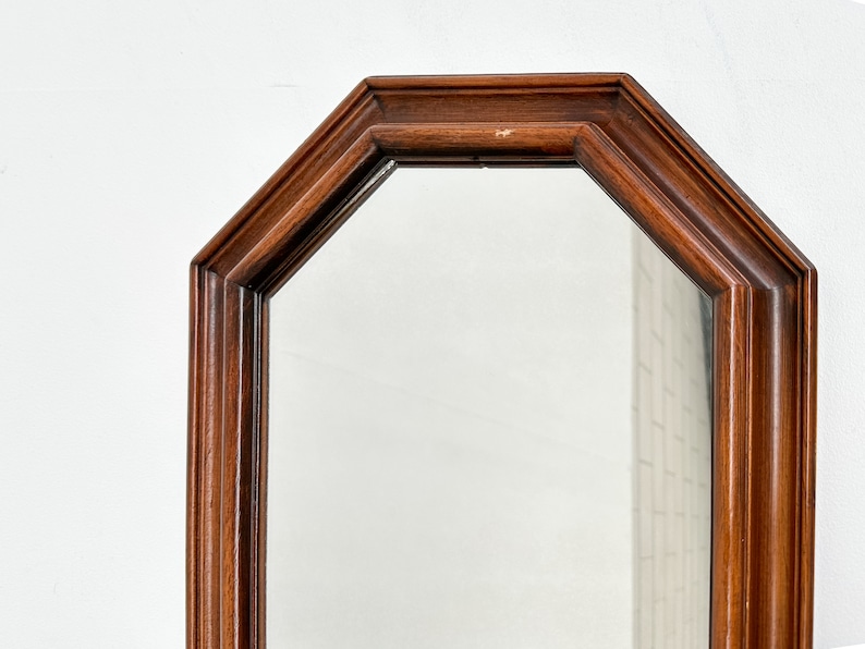May include: A wooden octagonal mirror with a simple, elegant design. The mirror has a dark brown wood frame and a clear glass surface.