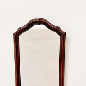 May include: A tall, wooden framed mirror with a curved top and a dark mahogany finish.