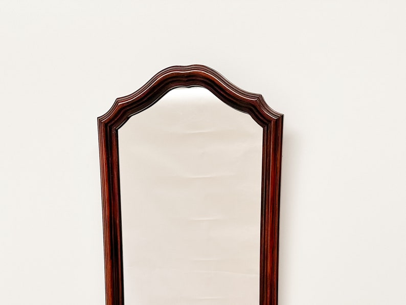 May include: A tall, wooden framed mirror with a curved top and a dark mahogany finish.