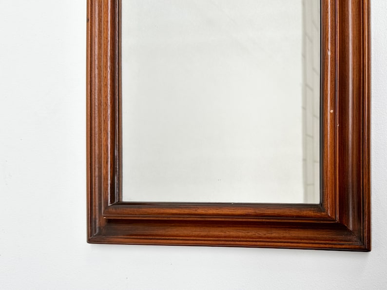 May include: A rectangular mirror with a dark wood frame. The frame has a simple, elegant design with multiple layers of molding.