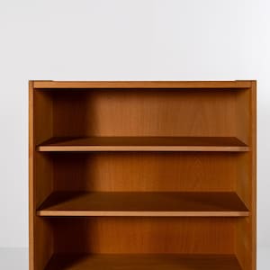 Puede incluir: Una estanter&iacute;a de madera con tres estantes. La estanter&iacute;a es de madera de color marr&oacute;n claro y tiene un dise&ntilde;o simple y rectangular. Los estantes est&aacute;n espaciados uniformemente y parecen estar vac&iacute;os. El fondo es una pared blanca lisa.