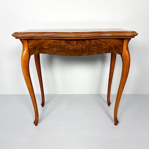 Puede incluir: Una mesa de madera con un acabado marrón marmoleado y una tapa rectangular. La mesa tiene cuatro patas con un diseño curvo.