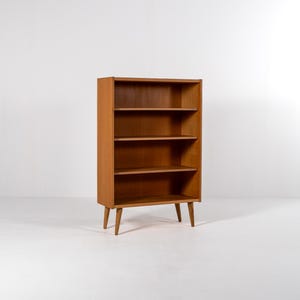 Puede incluir: Estanter&iacute;a de madera marr&oacute;n claro de estilo moderno de mediados de siglo. La estanter&iacute;a tiene cuatro estantes y se apoya en cuatro patas c&oacute;nicas. Los estantes est&aacute;n espaciados uniformemente. Mide unos 120 cm de alto.