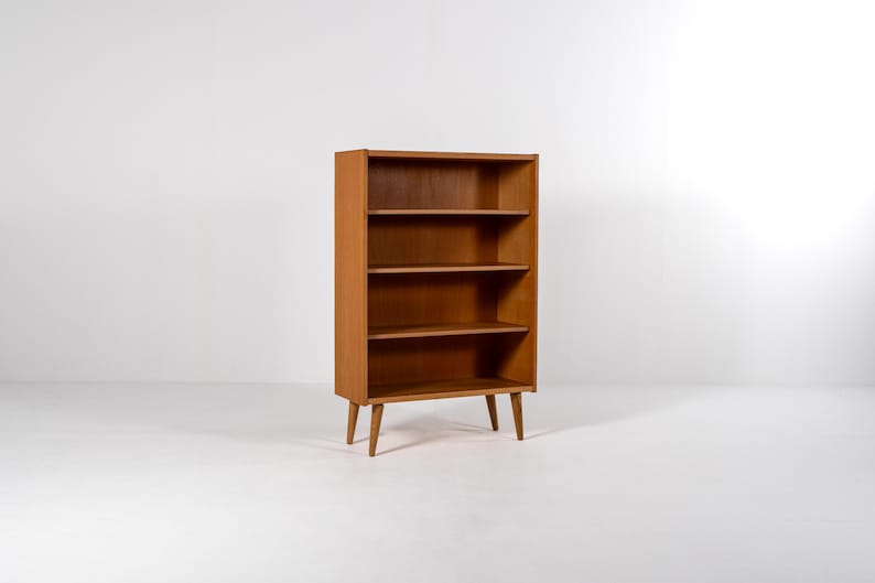 Puede incluir: Estanter&iacute;a de madera marr&oacute;n claro de estilo moderno de mediados de siglo. La estanter&iacute;a tiene cuatro estantes y se apoya en cuatro patas c&oacute;nicas. Los estantes est&aacute;n espaciados uniformemente. Mide unos 120 cm de alto.