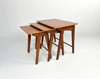 Puede incluir: Conjunto de tres mesas nido de madera con acabado natural. Las mesas son rectangulares y tienen un diseño sencillo y moderno de mediados de siglo.