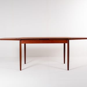 May include: A mid-century modern wooden dining table with a reddish-brown finish. The table has a rectangular top with two drop leaves extended, and four tapered legs. The table is approximately 183 cm long when fully extended.
