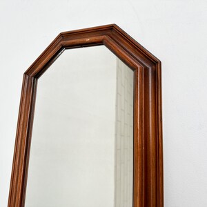 May include: A tall, octagonal mirror with a dark wood frame. The mirror is reflecting a white wall.