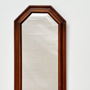 May include: A tall, rectangular mirror with a dark wood frame. The frame has an octagonal shape at the top and bottom.