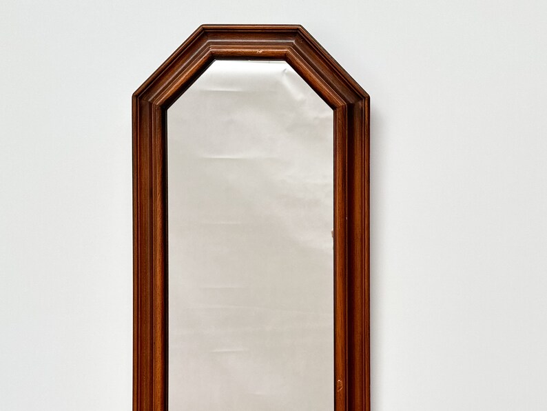 May include: A tall, rectangular mirror with a dark wood frame. The frame has an octagonal shape at the top and bottom.