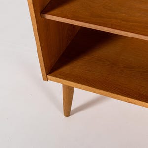 Puede incluir: Estanter&iacute;a de madera de estilo moderno de mediados de siglo, con dos estantes y patas c&oacute;nicas. La madera de color marr&oacute;n claro tiene un dise&ntilde;o sencillo y minimalista. Los estantes est&aacute;n soportados por un marco que se inclina ligeramente hacia afuera.