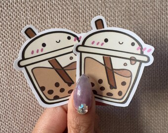 Puede incluir: Dos pegatinas de té de burbujas de dibujos animados marrones y blancas con una cara linda y mejillas rosadas. Las pegatinas están sobre un fondo beige.