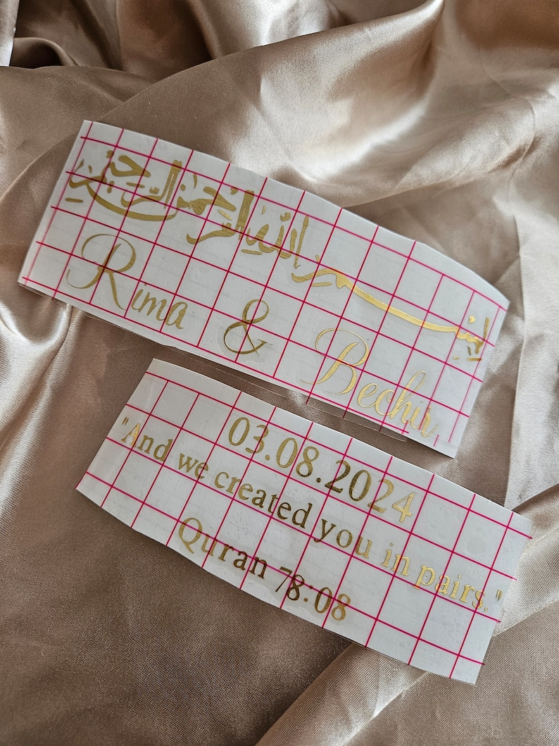 May include: Two rectangular adhesive vinyl decals with gold lettering on a white grid transfer paper. The top decal features Arabic calligraphy and the names Rima & Bechir. The bottom decal displays the date 03.08.2024 and the text And we created you in pairs. Quran 78:08.