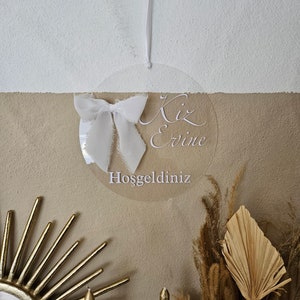 May include: A white acrylic circle with the text "Kız Evine Hoşgeldiniz" which translates to "Welcome to the Girl's Home" in English. The circle is hanging from a white string and has a white bow attached to it.