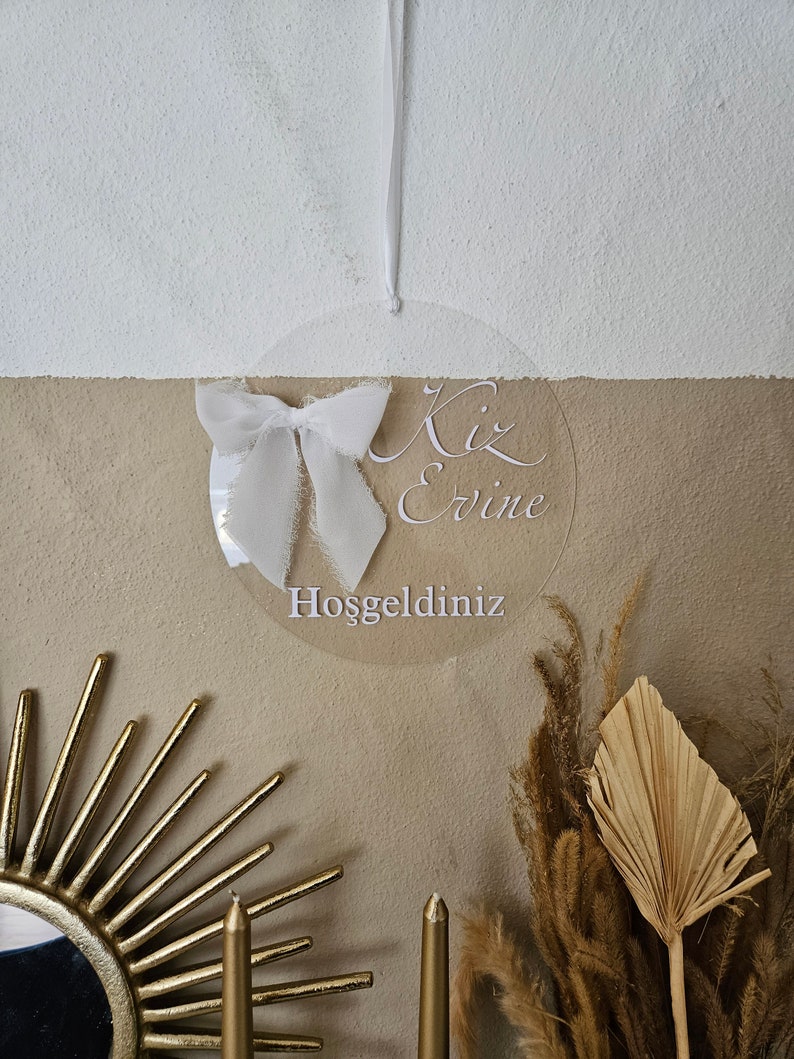 May include: A white acrylic circle with the text "Kız Evine Hoşgeldiniz" which translates to "Welcome to the Girl's Home" in English. The circle is hanging from a white string and has a white bow attached to it.