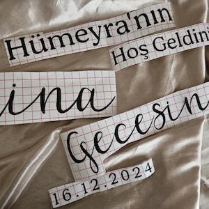 May include: Black vinyl lettering decals on a white grid transfer paper. The text reads H&uuml;meyra'nın Hoş Geldiniz Kına Gecesine and the date 16.12.2024. The decals feature a mix of bold serif and elegant script fonts for custom application.