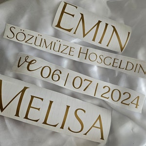 May include: Four separate adhesive vinyl decals featuring gold lettering on a white backing. The text reads EMIN, S&Ouml;Z&Uuml;M&Uuml;ZE HOSGELDINIZ, ve 06 | 07 | 2024, and MELISA. The decals are arranged in a stack, showcasing a mix of serif and script fonts.