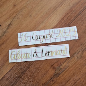 May include: Two rectangular adhesive vinyl decals with a red grid transfer paper backing. The top decal features the gold text 16. August 2025. The bottom decal displays the gold names Alicia & Lennart in a cursive script font style.