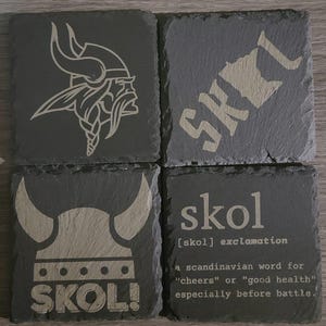 May include: Four black slate coasters featuring a Viking helmet and the word "SKOL!" engraved on them. The coasters also include the definition of the word "skol" as a Scandinavian word for "cheers" or "good health", especially before battle.