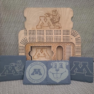 May include: A wooden game board with a Minnesota Golden Gophers logo and a gopher mascot. The board is made of light wood and has a dark brown stain. The game board is surrounded by four slate coasters with the Minnesota Golden Gophers logo and a gopher mascot.