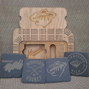 May include: A wooden game board with a Minnesota Wild logo and a slate game piece with the Minnesota Wild logo. The game board is made of wood and has a light brown finish. The game piece is made of slate and has a dark gray finish.