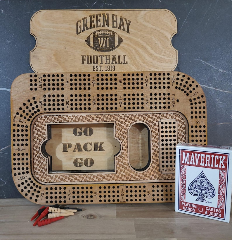 May include: A wooden game board with a green and white football design. The board is labeled "Green Bay WI Football Est. 1919". The board has a grid of holes and a "Go Pack Go" inscription.
