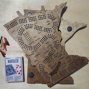 May include: A wooden game board shaped like the state of Minnesota with holes for pegs. The board is brown and has the names of cities and towns in Minnesota printed on it. The game is called "Minnesota Trivia".