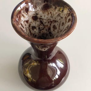 May include: A dark brown ceramic vase with a rounded base and a flared rim. The rim's interior has a speckled white and brown pattern. The vase's surface is glossy and reflective, with a vintage design. The vase is approximately 15 cm tall.